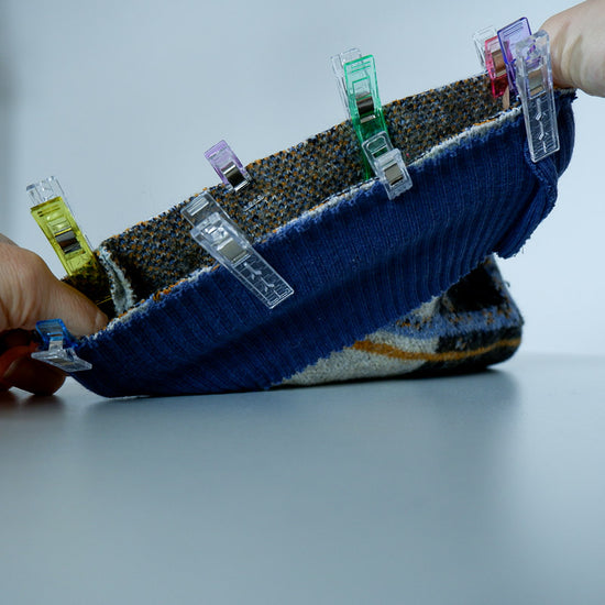Close-up of a water bottle holder with various sewing clips attached, held by a hand against a light gray background.