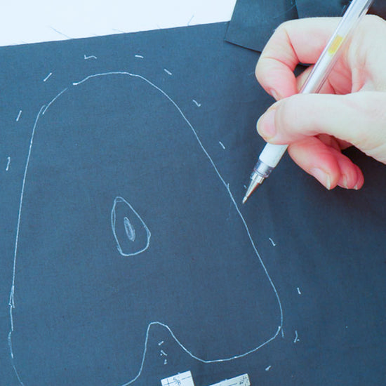 Hand holding a heat erasable pen over a dark piece of fabric with a white outline of the letter A