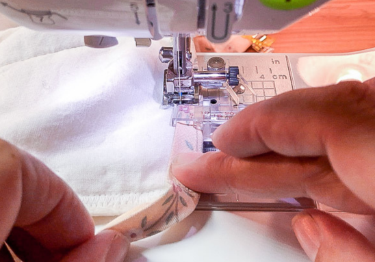 hands guiding the bias tape on der a binder presser foot