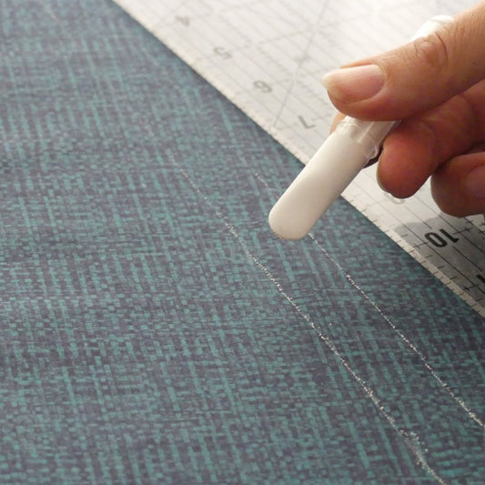 Detail of the chalk wheel of a white chalk marker with two thin lines drawn on fabric and a ruler