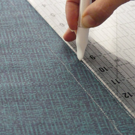 Drawing a line with a white chalk marker and a quilt ruler on dark fabric