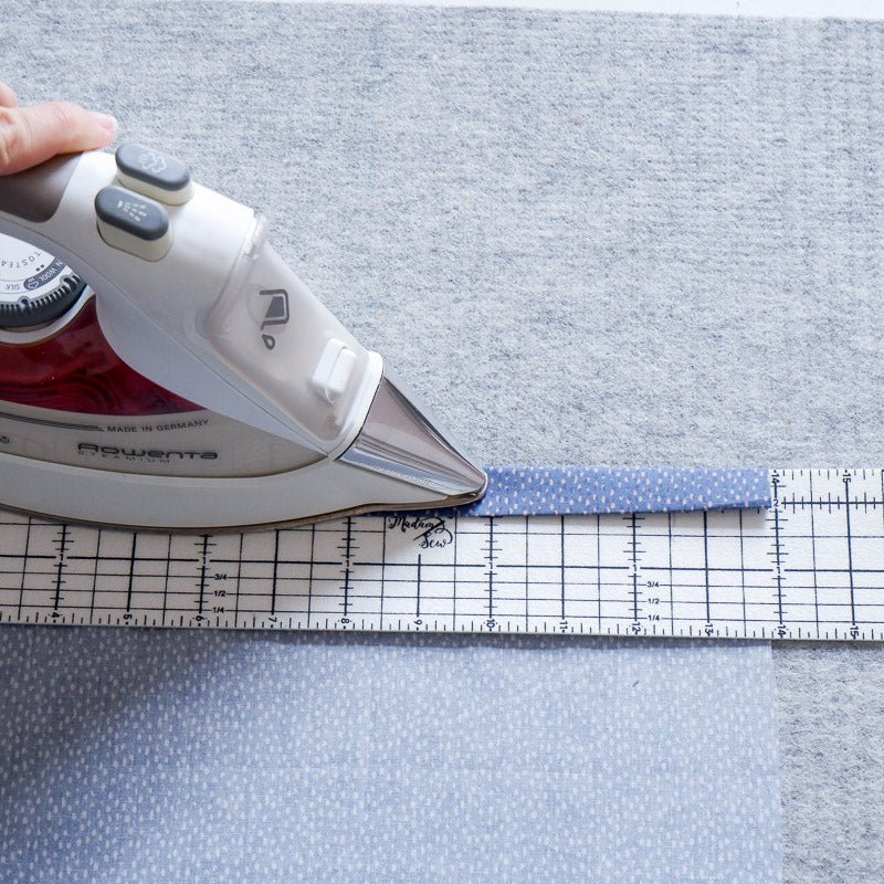 Someone uses a hot hem ruler and iron to iron a hem on dotted fabric
