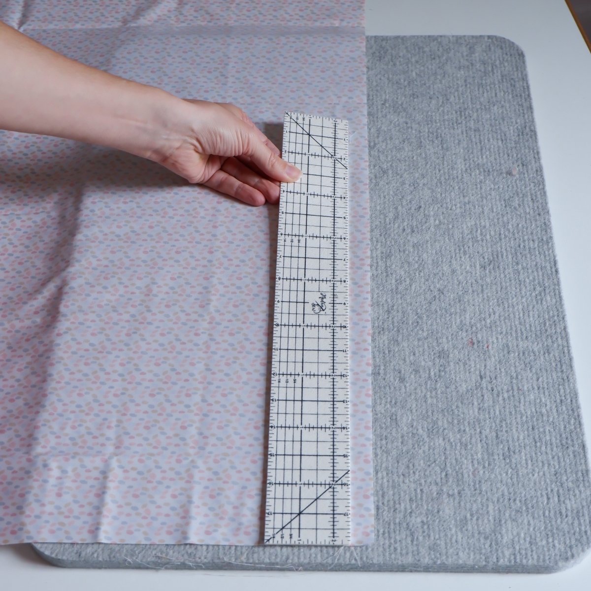 Someone using a Hot Hem Ruler for Sewing pastel fabric on a wool pressing mat