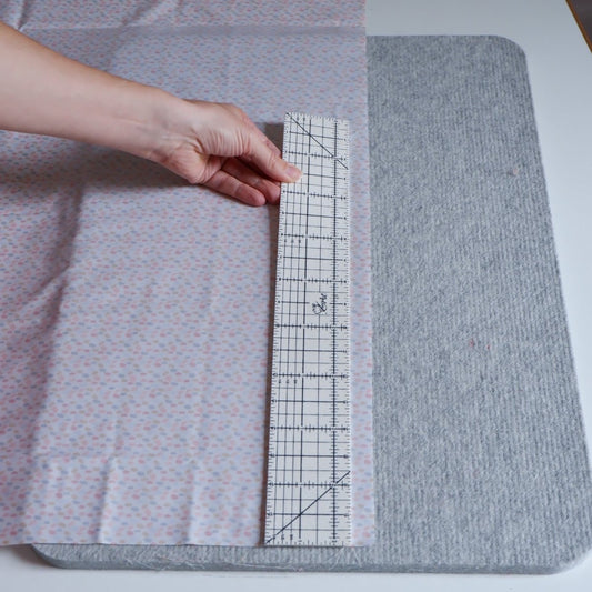 Someone using a Hot Hem Ruler for Sewing  pastel fabric on a wool pressing mat