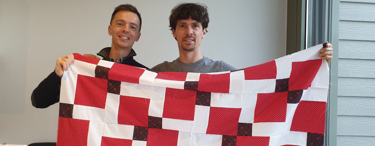 two men holding a handmade quilt top