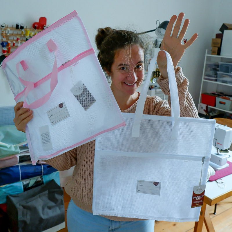 Women holding a white and a pink storage bag in a sewing room