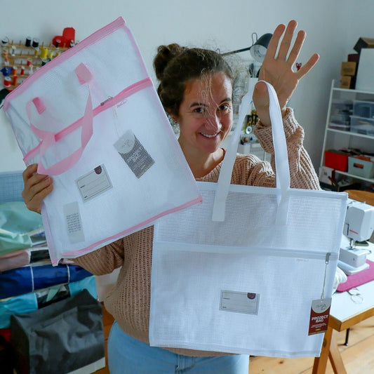 Women holding a white and a pink storage bag in a sewing room