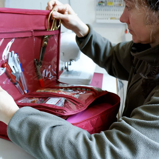 A woman grabbing fabric shears from a red multi-pocket sewing bag