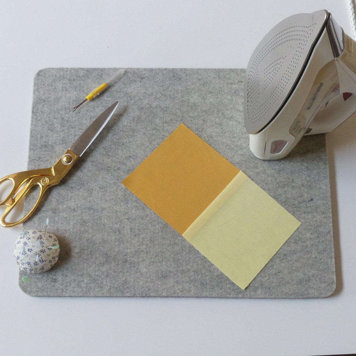 Wool Pressing Mat on a table with scissors, an iron, a pincushion, seam ripper and some fabrics