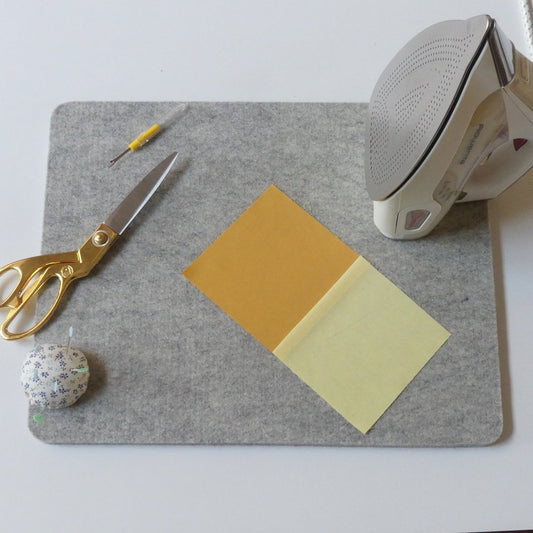 Wool Pressing Mat on a table with scissors, an iron, a pincushion, seam ripper and some fabrics