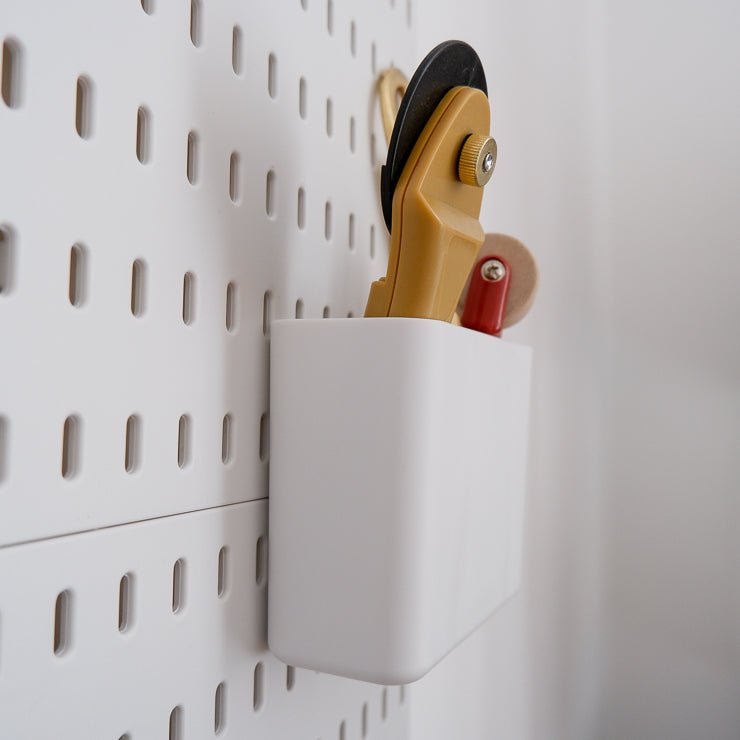 Side view of the three-compartment box for a MadamSew Pegboard with a rotary cutter attached to the wall