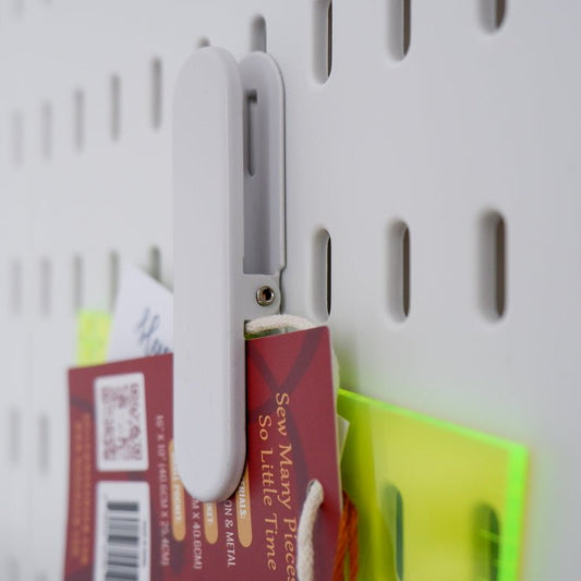 A clip hanging on a peg board holding a ruler and some cards