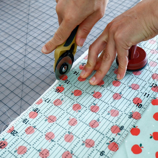 hands cut fabric with a rotary cutter and a ruler
