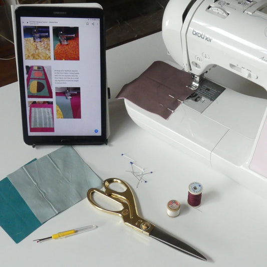 tablet on a tablet stand with a quilt tutorial next to a sewing machine on a craft table