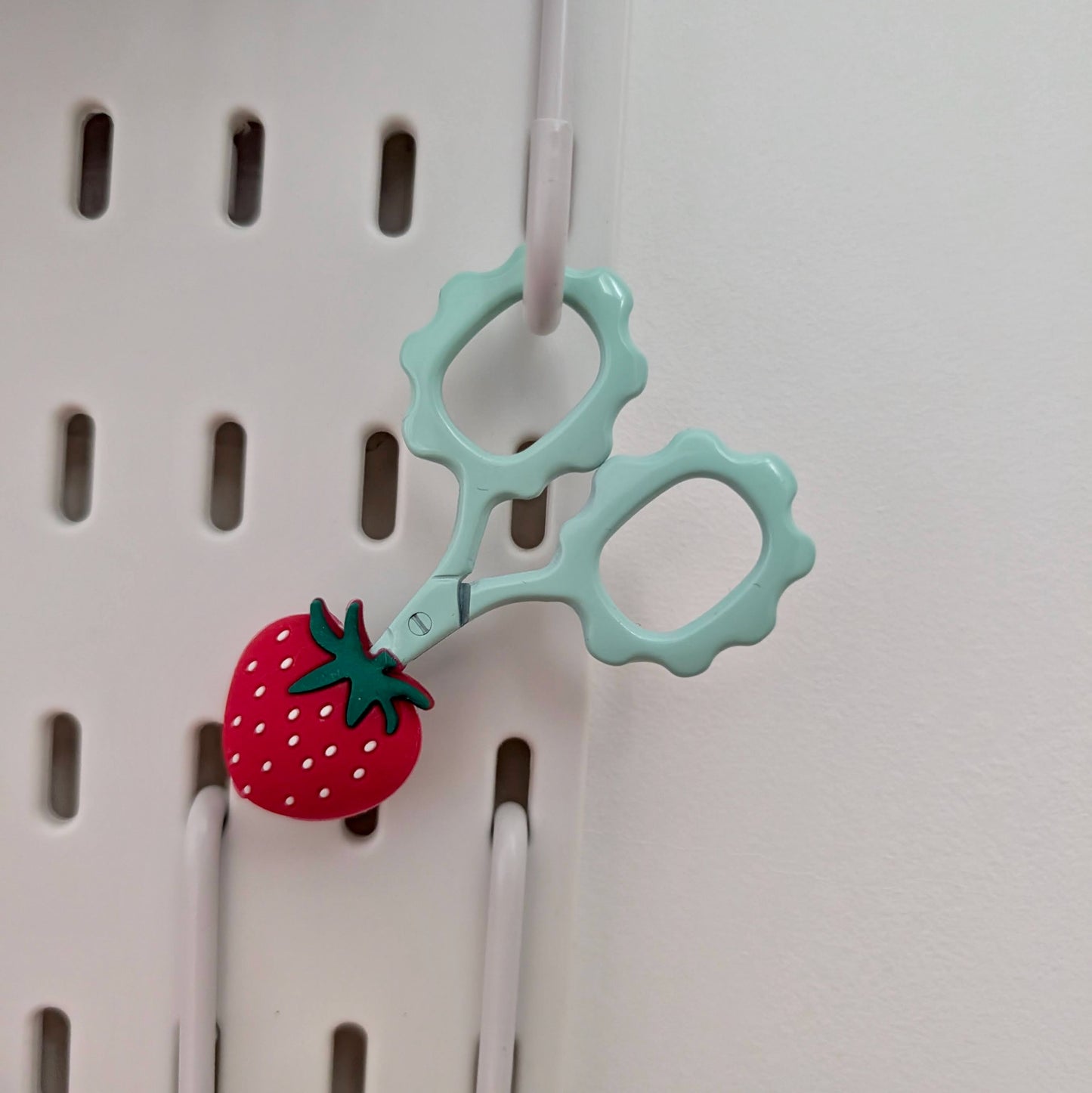 Teal snips with cover hanging up on pegboard