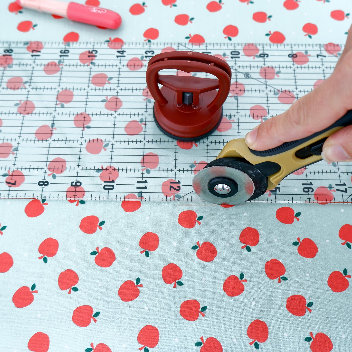 Fabric with red apple pattern being cut by a rotary cutter on a polka dot background