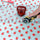 Fabric with red apple pattern being cut by a rotary cutter on a polka dot background