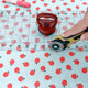 Fabric with red apple pattern being cut by a rotary cutter on a polka dot background