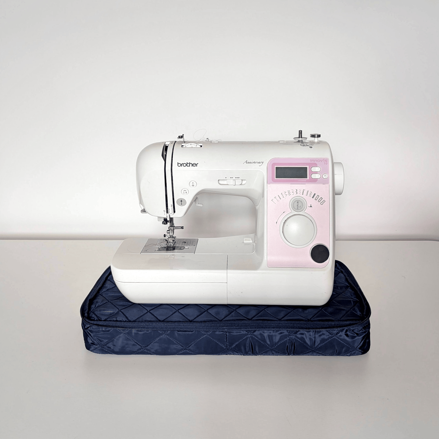 Animation of a sewing machine on a navy quilted base, covered into a zipped bag, then lifted by its strap
