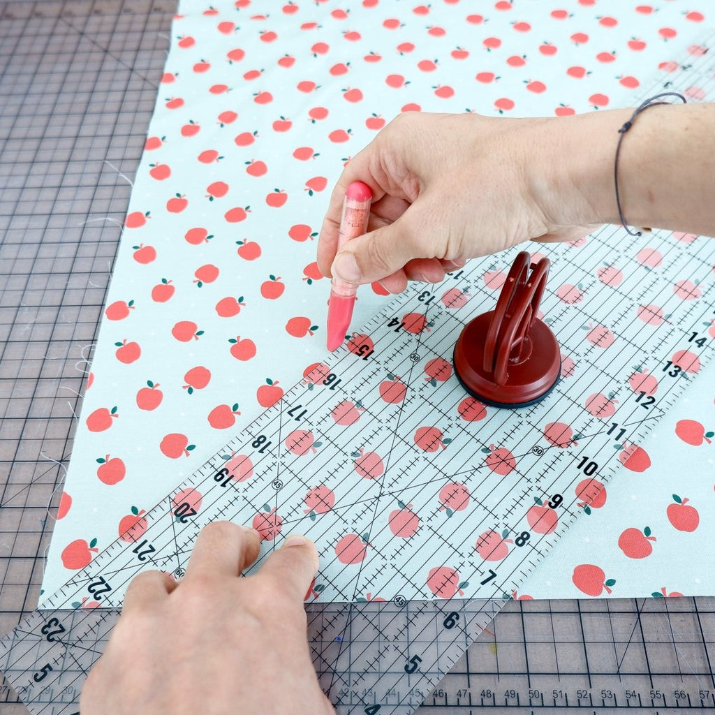 Hand drawing a line with a red chalk marker and a ruler on colorful fabric