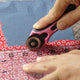 women using a pink 28 mm rotary cutter to cut red fabric with a ruler