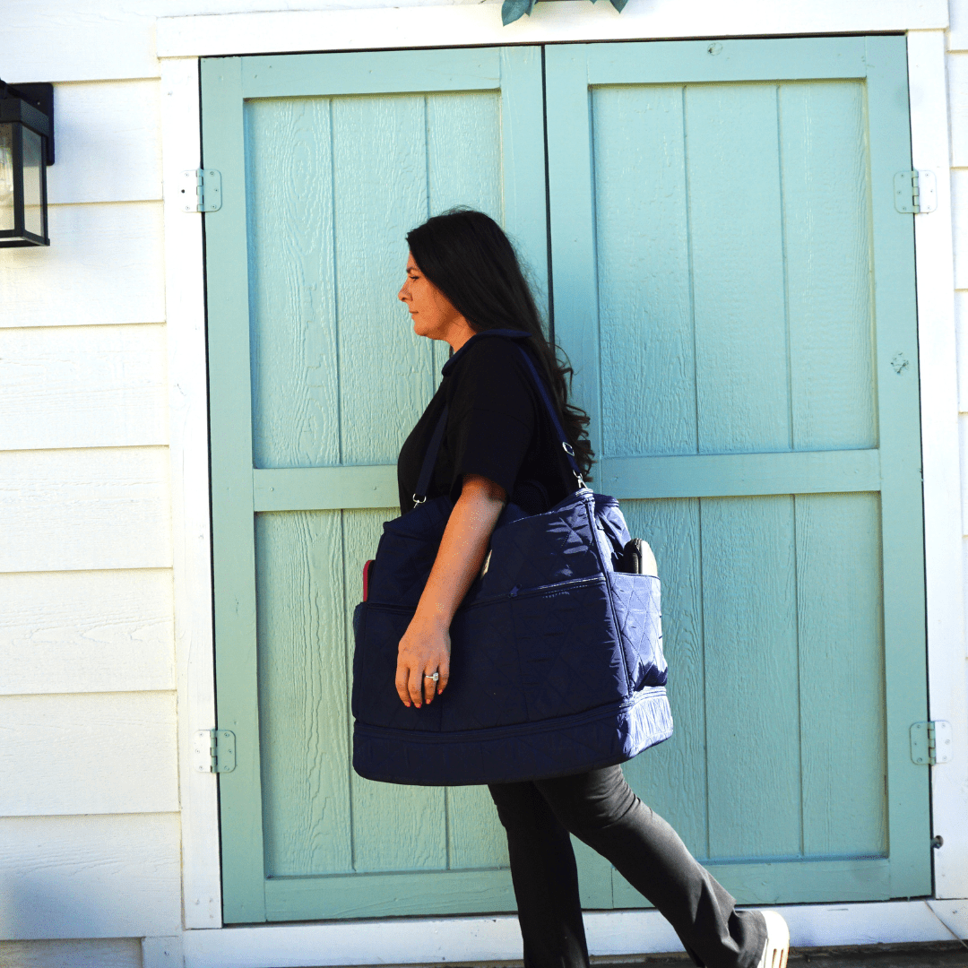Woman walking past pale green doors carrying a navy quilted sewing machine bag on her shoulder