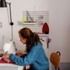 Woman in a sewing room sewing with a sewing machine with a peg board on the wall