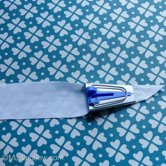 The point of a fabric strip coming out of the blue bias tape maker.