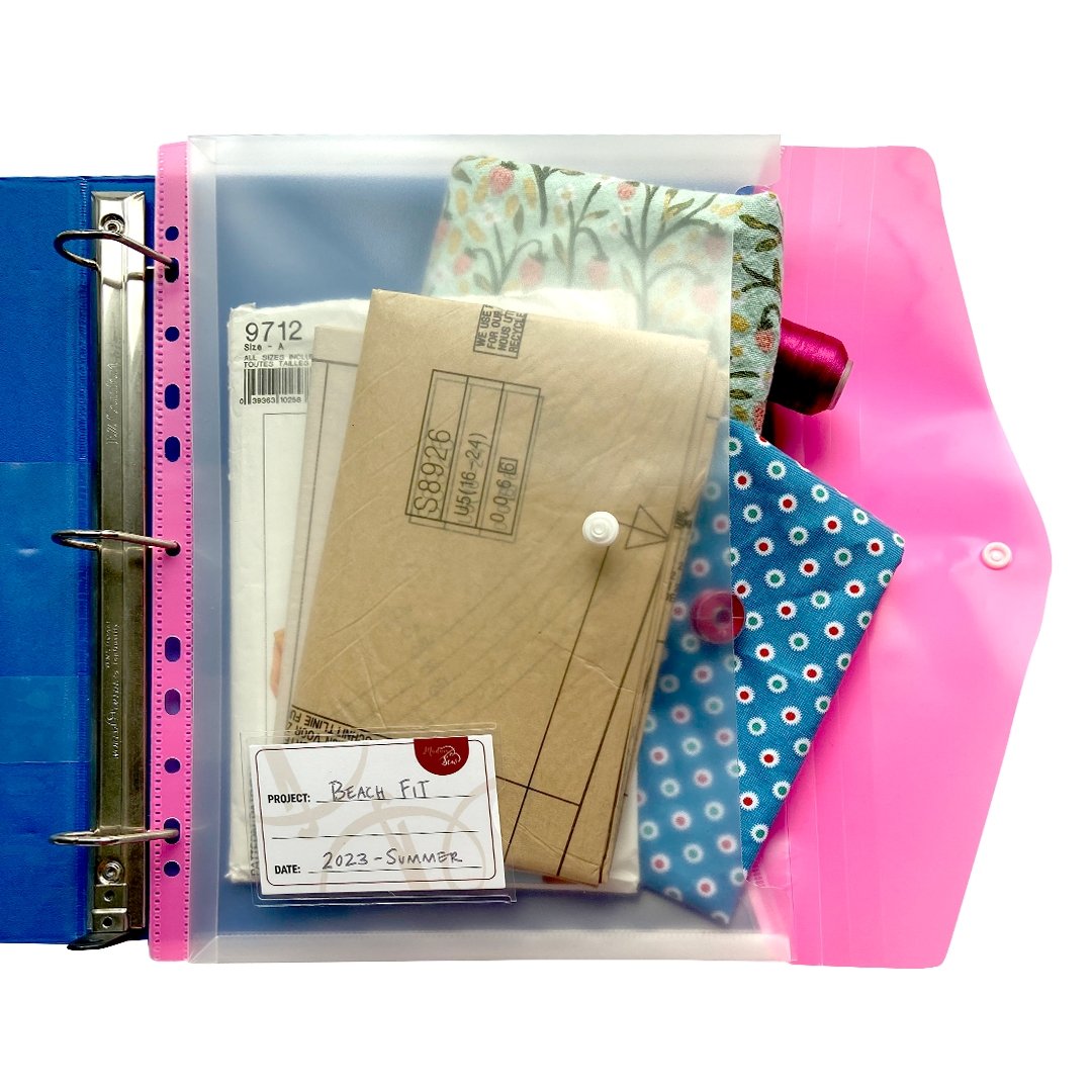 One organization sewing room binder pockets in color pink holding sewing patterns, fabric inserted into a blue binder.