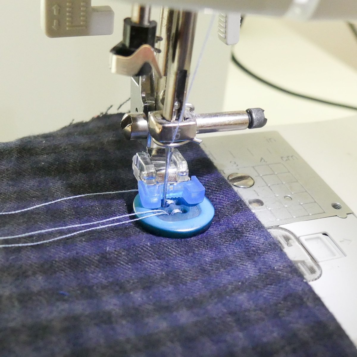 A sewing machine attachment sewing on a blue button on a garment, sewing machine close-up