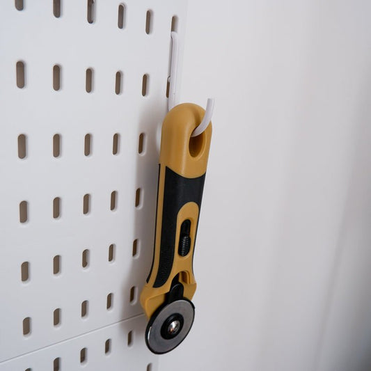 a C-hook on a peg board with a rotary cutter hanging on it
