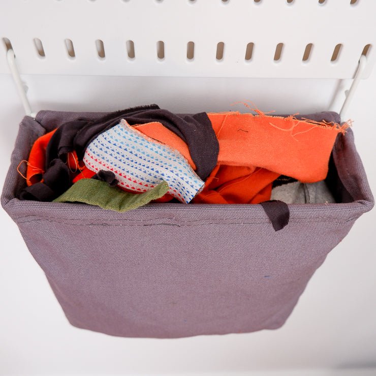 a canvas bag with fabric scraps hanging off a peg board