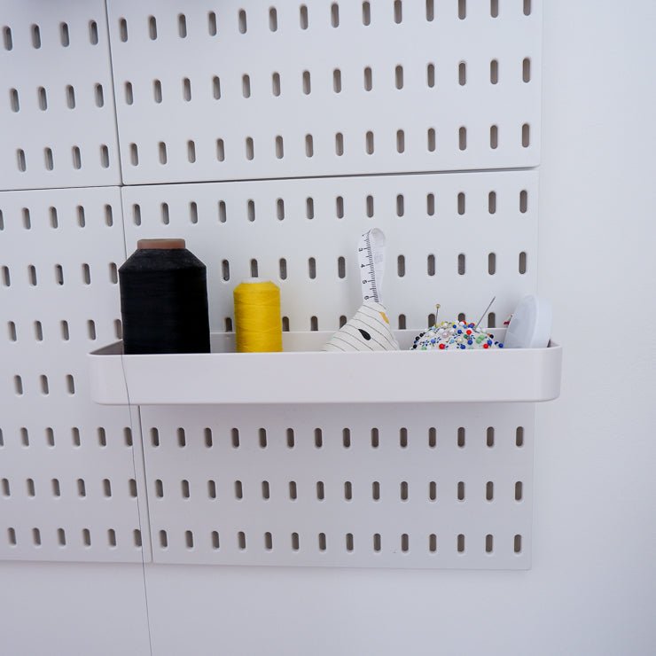 White long plastic tray attached to a peg board holding thread spools and other sewing notions