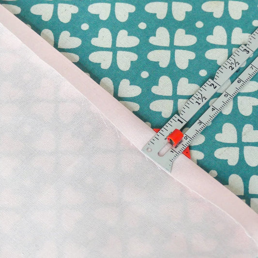 Sewing gauge measuring a hem of half an inch on pink fabric