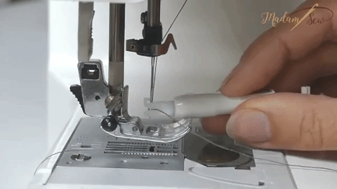 a hand shows how to use the needle threader tool on a sewing machine