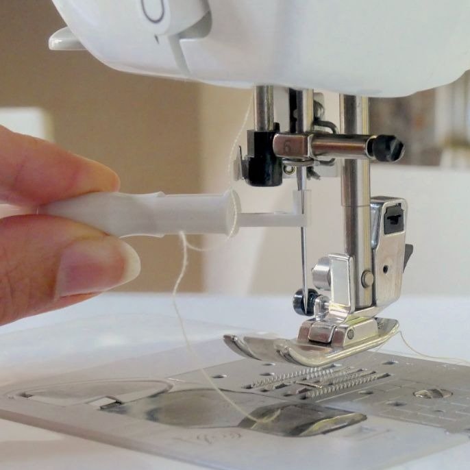 A hand holding the needle inserter tool and is installing a sewing machine needle
