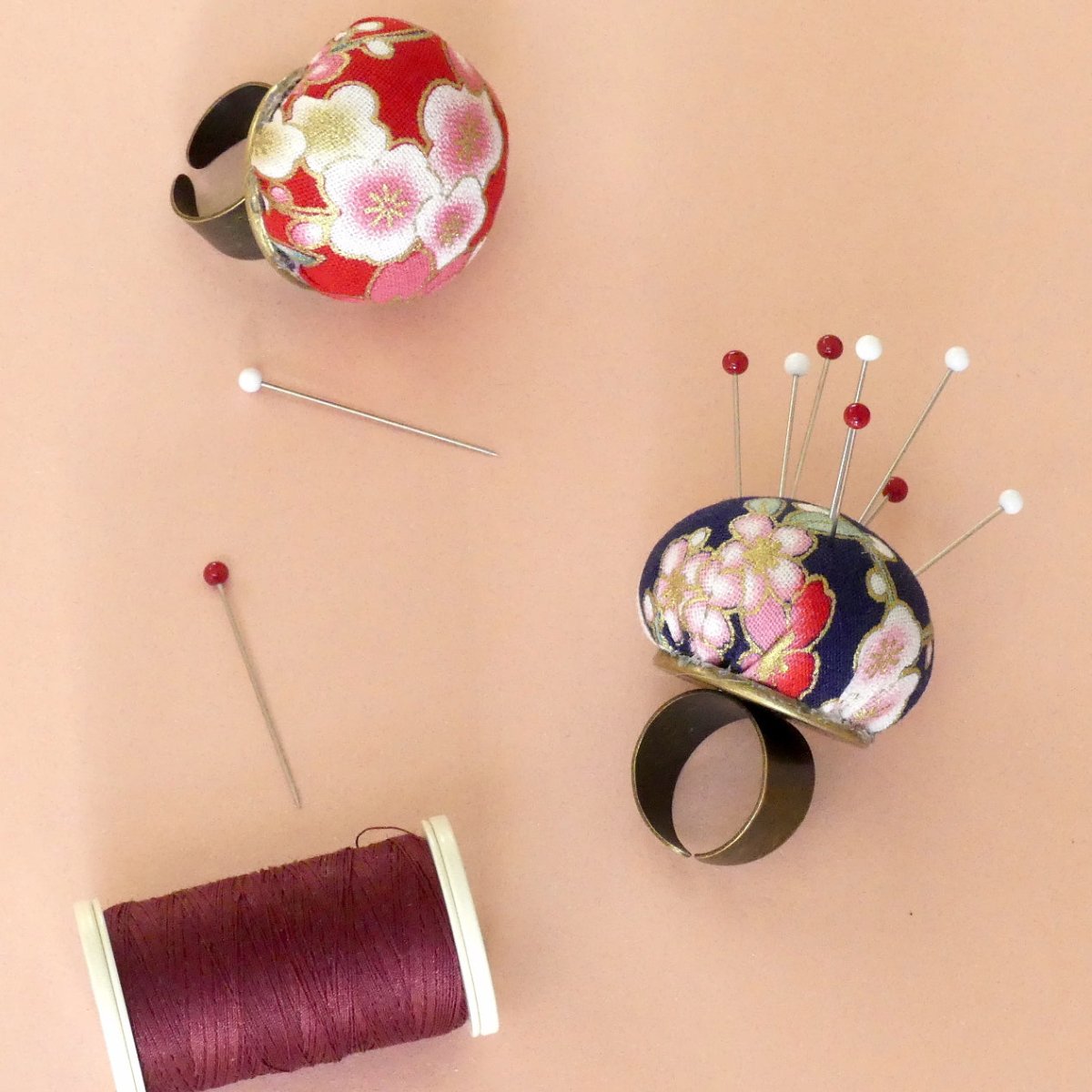 Ring Pin Cushion two-piece set with pins inserted and a maroon spool of thread