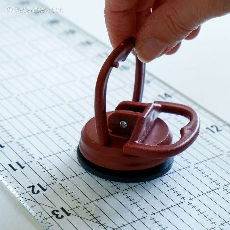 The Madam Sew Ruler Grip on a quilt ruler, hand holding the suction cup mechanism