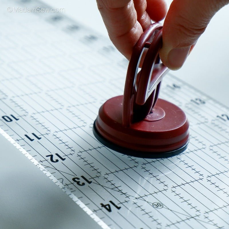 The Madam Sew Ruler Grip on a quilt ruler, hand closing the suction cup mechanism