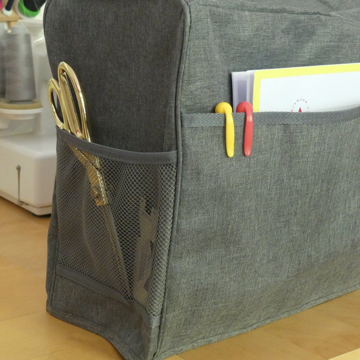 A grey sewing machine cover that protects a sewing machine from dust with side pockets
