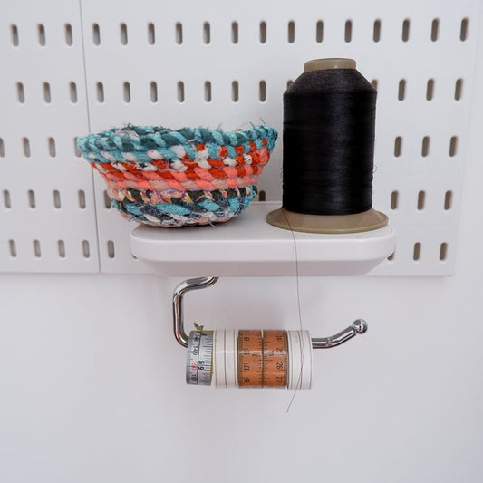 Spool Shelf on a peg board with a little basket a large thread cone and some craft tape