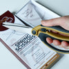 A hand showing the Madam Sew spring scissors in the closed position with the packaging in the back