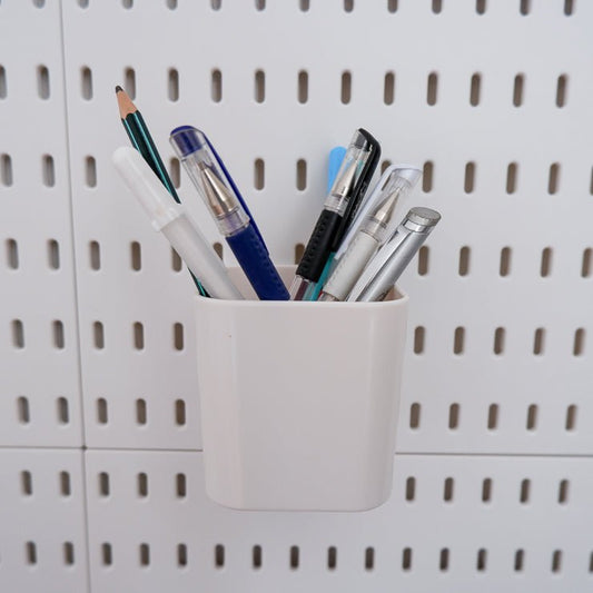 A white box on a peg board holding pens and fabric markers