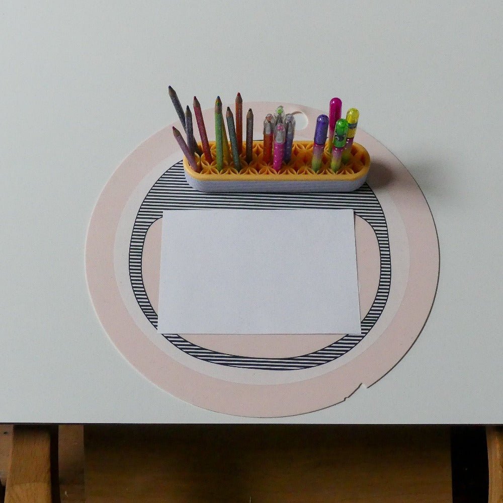 a pencil and marking pen holder on a table with a paper and a round coaster