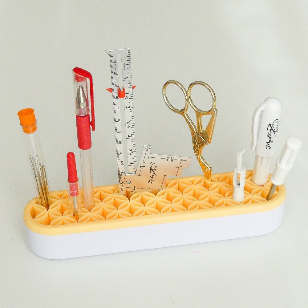 a yellow tool holder on a desk with sewing snips, fabric marker, a seam gauge, a seam rippen and needles